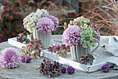 Autumn bouquets of chrysanthemums, hydrangeas and St. John's wort in grey cups, faded hydrangea blossoms and berries from the love pearl bush scattered on the table
