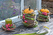 Patisson-Kürbisse und Kerze mit Grasmanschetten und Fruchtständen vom Pfaffenhütchen am Fenster