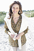 A long-haired woman wearing a floral shirt with a white jumper over his shoulders