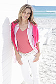Langhaarige Frau in Longbluse und mit pink Pullover über den Schultern am Strand
