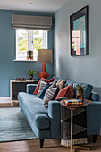 Rust-red scatter cushions on blue sofa against pale blue wall in living room