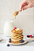 Pouring honey pancakes with berries and butter