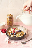 Pouring milk to granola with nuts, oats and berries