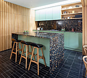 Black terrazzo island counter and green cabinets in open-plan kitchen