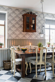Holztisch mit Stühlen und antiker Wandschrank in der Küche mit grauer Holzverkleidung und Tapete