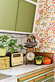 Vintage-style accessories in retro kitchen with green cabinets and floral wallpaper