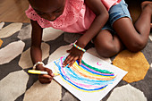 Girl drawing multicolour rainbow with marker on rug