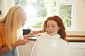 Teenage girl cutting hair for worried friend in kitchen