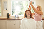 Mother cutting hair for preteen daughter in kitchen