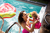 Happy mother lifting daughter into summer swimming pool