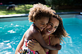 Happy mother and daughter hugging at summer poolside