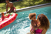 Family playing in sunny summer swimming pool