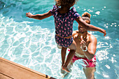 Daughter jumping into arms of father in swimming pool