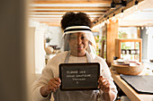 Shop owner in face shield holding hand sanitizer sign