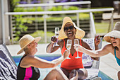 Senior women friends drinking champagne at summer poolside