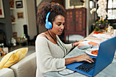 Woman with headphones working at laptop on dining table