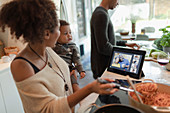 Family cooking dinner and video chatting by digital tablet