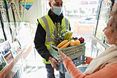 Woman receiving grocery delivery from delivery man in mask