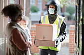 Woman receiving parcels from delivery man in face mask