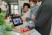 Family video chatting at digital tablet and cooking dinner