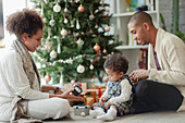 Parents helping baby daughter open Christmas gifts by tree