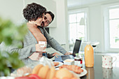 Couple working at laptop in morning kitchen