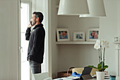 Man talking on smart phone at dining room window