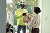 Woman receiving food delivery from man in face mask