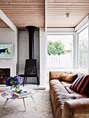 Brown leather sofa, coffee table and wood-burning stove in living room with white painted brick wall