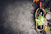 Flasche Rotwein mit Trauben und Blättern im Dekantierkörbchen