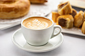 Kaffee mit kunstvollem Milchschaum-Muster und süßem Gebäck