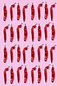 Vier Reihen rote Chilischoten auf rosa Untergrund