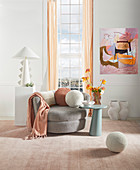 Feminines Wohnzimmer in Pastell mit grauem Sessel vorm Fenster