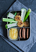A breakfast box with bread bites, celery, apple sauce and biscuits