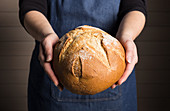 Woman holds freshly baked bread loaf
