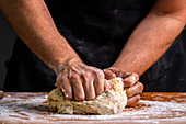 Hands kneading and rolling pile of dough for bread