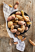 Colourful potatoes in a ceramic bowl with a tea towel on a wooden background