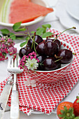 Bowl of 'Schwarze Knorpelkirsche' cherries with love-in-a-mist and pink yarrow flowers