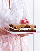 Frau hält quadratischen Schokoladen-Biskuitkuchen mit Cremefüllung