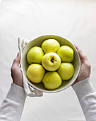 Hands holding a bowl with yellow apples