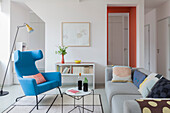Blauer Ohrensessel, Coffeetable und graues Sofa in offenem Wohnraum