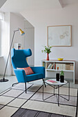 Blue wing-back chair, standard lamp and coffee table in open-plan interior