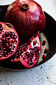 Pomegranates, whole and halved, in a black bowl