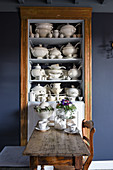 Wooden table and chair in front of shelves holding old white crockery
