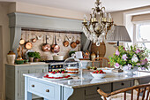 Kuchen auf Küchentisch mit Marmor-Arbeitsplatte, darüber französischer Kronleuchter, Kupferpfannen an der Wand
