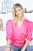 Junge blonde Frau in pink Wickelbluse mit Puffärmel und Jeans