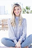 A young blonde woman wearing a blue-and-white patterned top and jeans