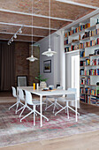 Dining table with chairs, pendant lamp above and bookcase in open plan living room with high ceiling