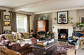 Buttoned chairs at lit fireside with animal skin on sofa and black travelling chest