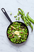 Fried broad beans with bacon in a pan